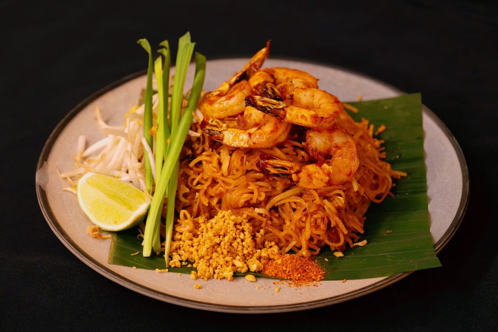 Pad Thai with jumbo shrimp, lime, chive and crushed peanuts on banana leaf